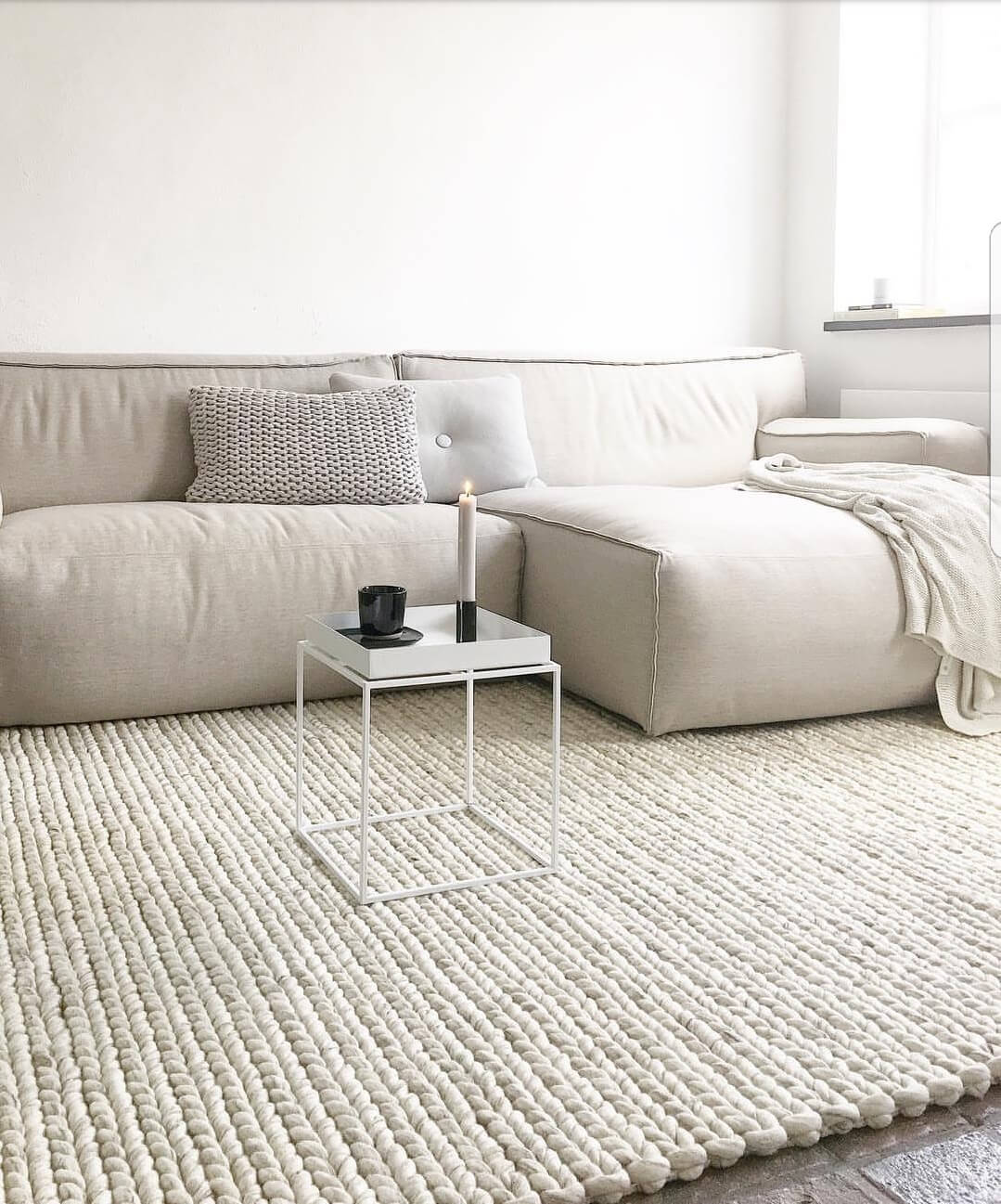 Grof wollen vloerkleed creme onder een bank
